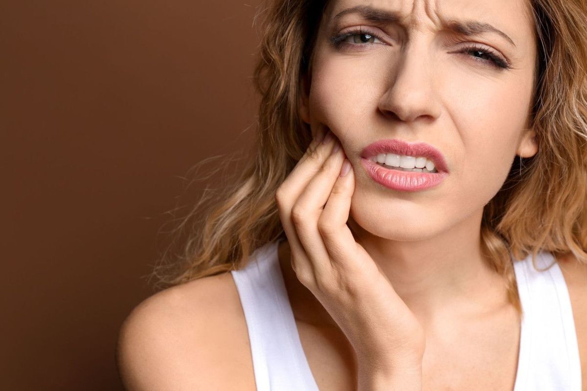 Is Your Tooth in Trouble Woman with tooth pain holding her cheek against brown background.
