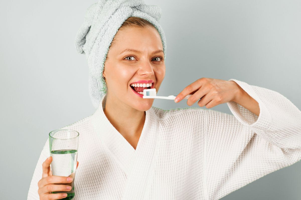 Refresh Your Morning Dental Care Routine Young woman brushing her teeth while holding a glass of water after her morning dental routine.