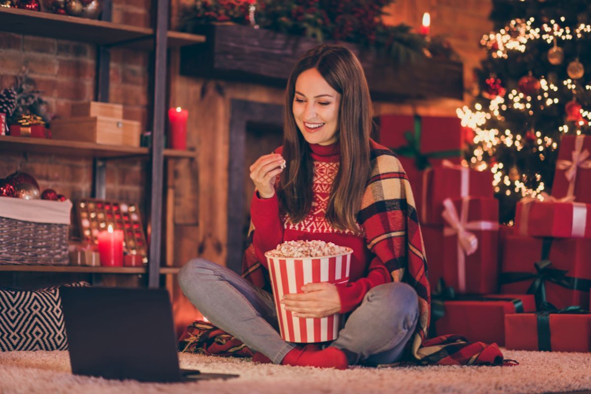 5 Holiday Treats that Support Your Dental Health Woman enjoying popcorn while watching holiday content on laptop in festive setting.