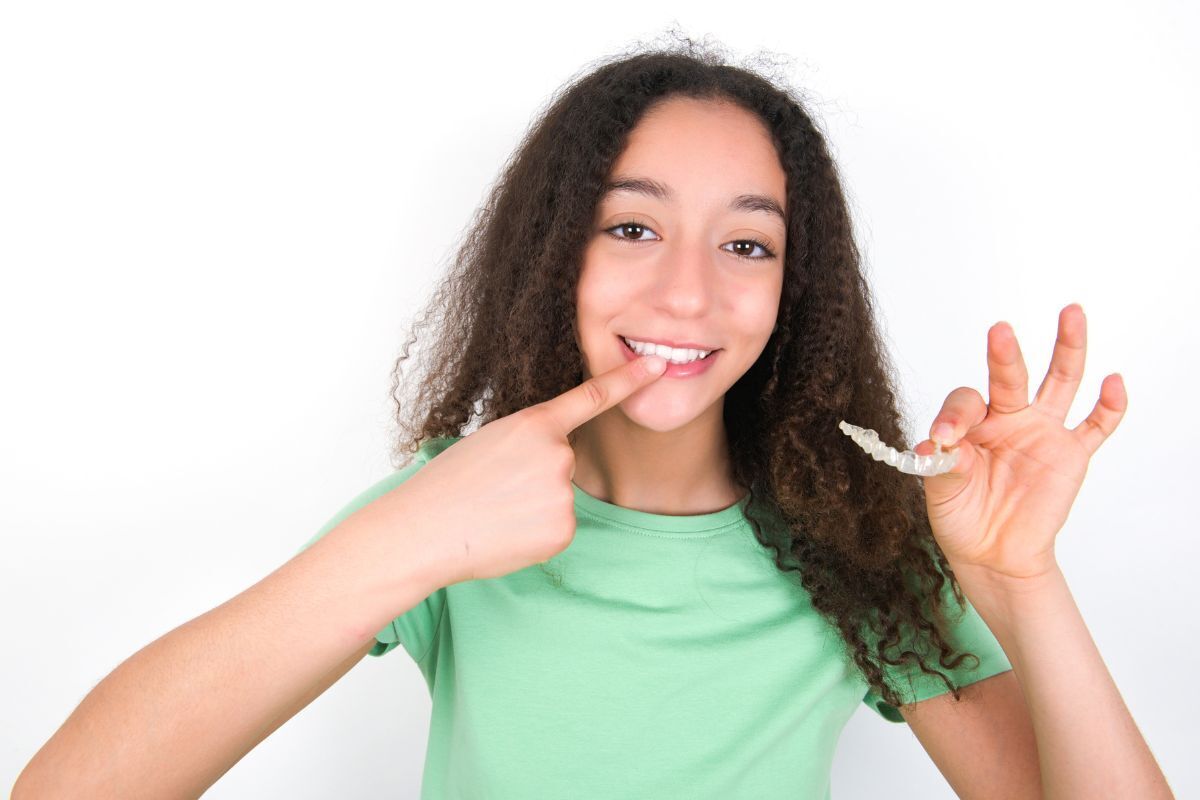 Is Your Teen Ready for Invisalign Smiling teen girl pointing to her clear Invisalign aligners during orthodontic treatment.
