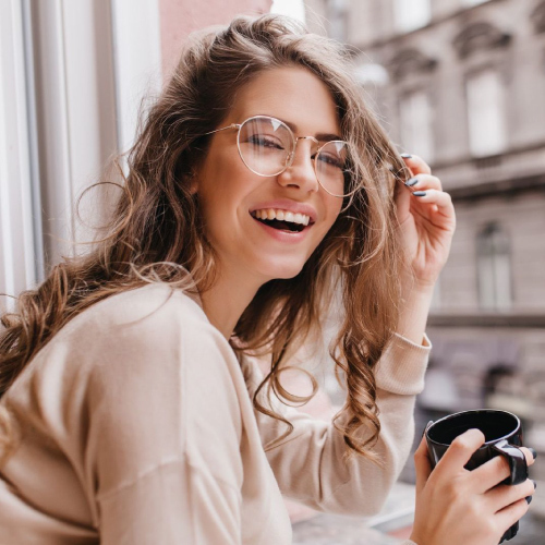 Close-up portrait of laughing brunette girl in beige sweater drinking coffee on city background.