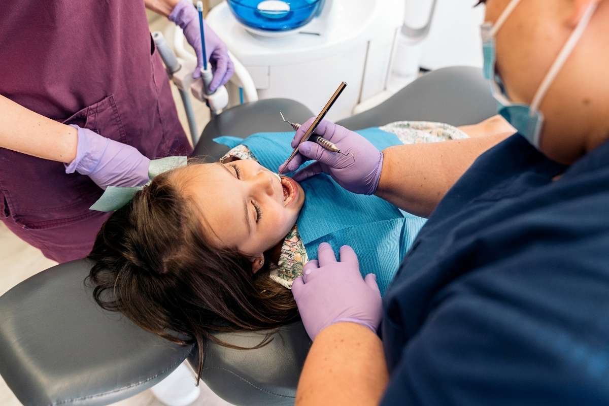 Knocked Out Tooth Treatment Young patient receiving dental examination and treatment in chair with gloved dentist and assistant.